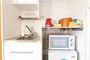 A compact kitchenette with a sink, a microwave, and a small shelf with a kettle and a box. - COZY TOKYO (Tokyo)