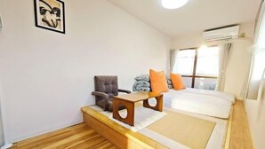 A bedroom with a bed, a chair, a small table, and a window with curtains.