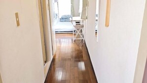 A narrow hallway with wooden flooring leading to a room with a bed and a desk.