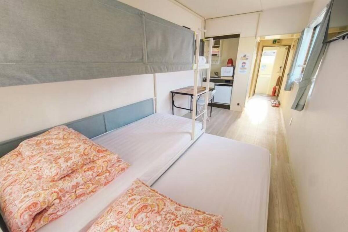 A narrow corridor with a bed on the left, a desk with a chair, and a kitchenette area.
