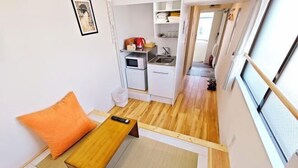 A compact room with a bed, a small table, a kitchen area, and a window.