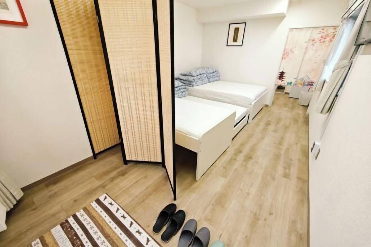A room with a bed, a small table, a chair, a wall-mounted TV, and a window.