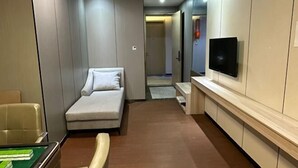 Ein Hotelzimmer mit Sofa, Flachbildfernseher an der Wand, einem kleinen Tisch und einem Sessel.