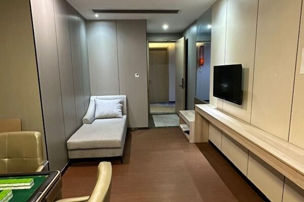 A hotel room with a sofa, a flat-screen TV mounted on the wall, a small table, and a chair. - Fucheng International Hotel (Vientiane)