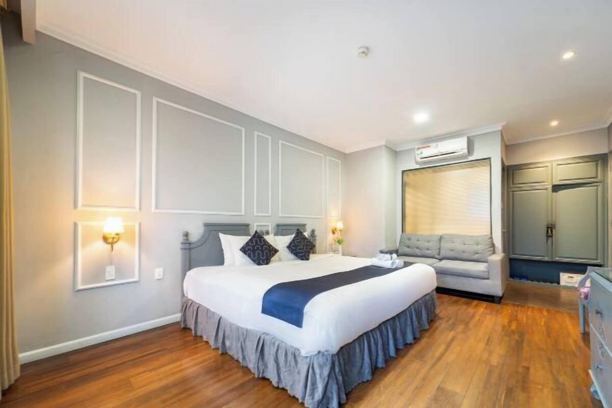A hotel room with a large bed, a sofa, a dresser, and a wall-mounted air conditioning unit.