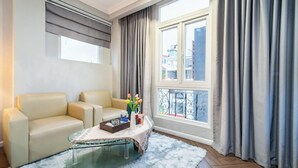 Una sala de estar moderna con un sofá, una mesa de centro de vidrio, una ventana con cortinas y vistas a edificios.