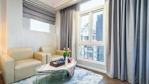 En moderne stue med sofa, glasbord og udsigt til bygninger gennem et vindue med gardiner.