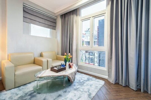 Una sala de estar moderna con un sofá, una mesa de centro de vidrio y vistas a edificios a través de una ventana con cortinas.