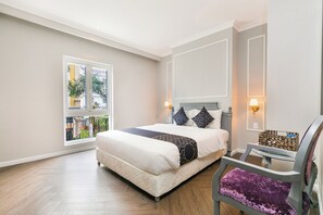 Habitación de hotel con cama, lámparas de noche, una silla, ventana con vistas y una mesita.
