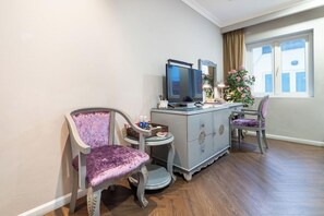 Una habitación con televisión, dos sillas, una mesita con objetos y una ventana con cortinas.