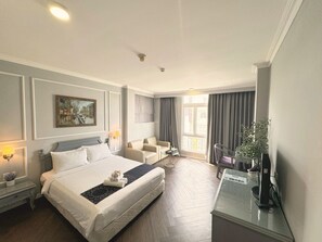 Habitación de hotel con una cama grande, zona de estar con sofá y sillones, una mesita y un televisor sobre un mueble.