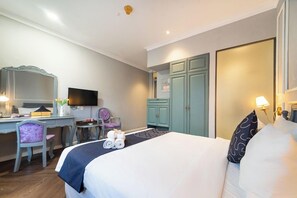 Una habitación de hotel con cama, escritorio, silla, televisor, armario y espejo.