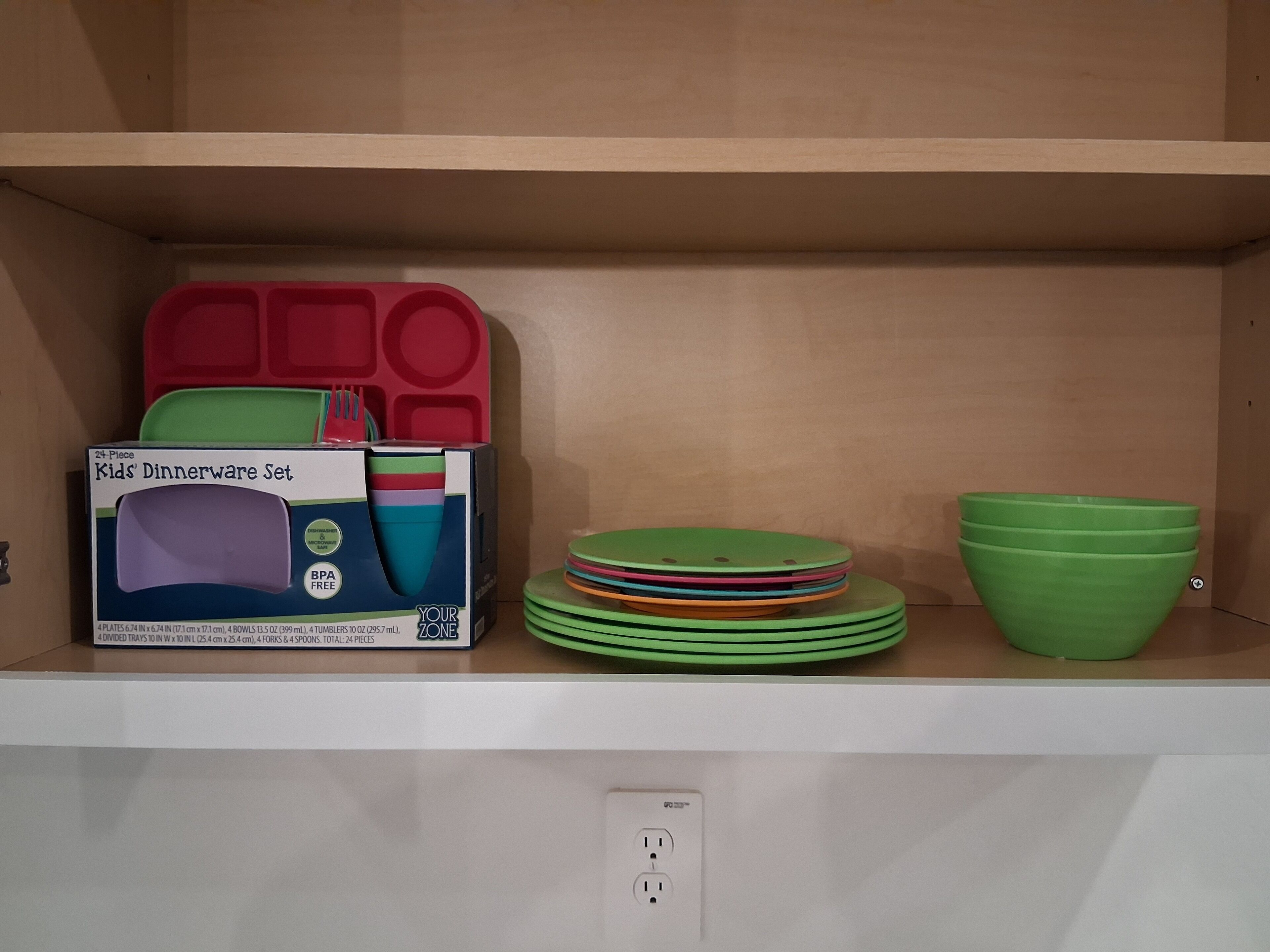 A shelf with a box of kids' dinnerware set, stacked plates, and a green bowl.