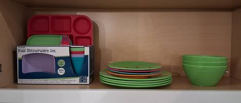 A shelf with a box of kids' dinnerware set, stacked plates, and a green bowl.