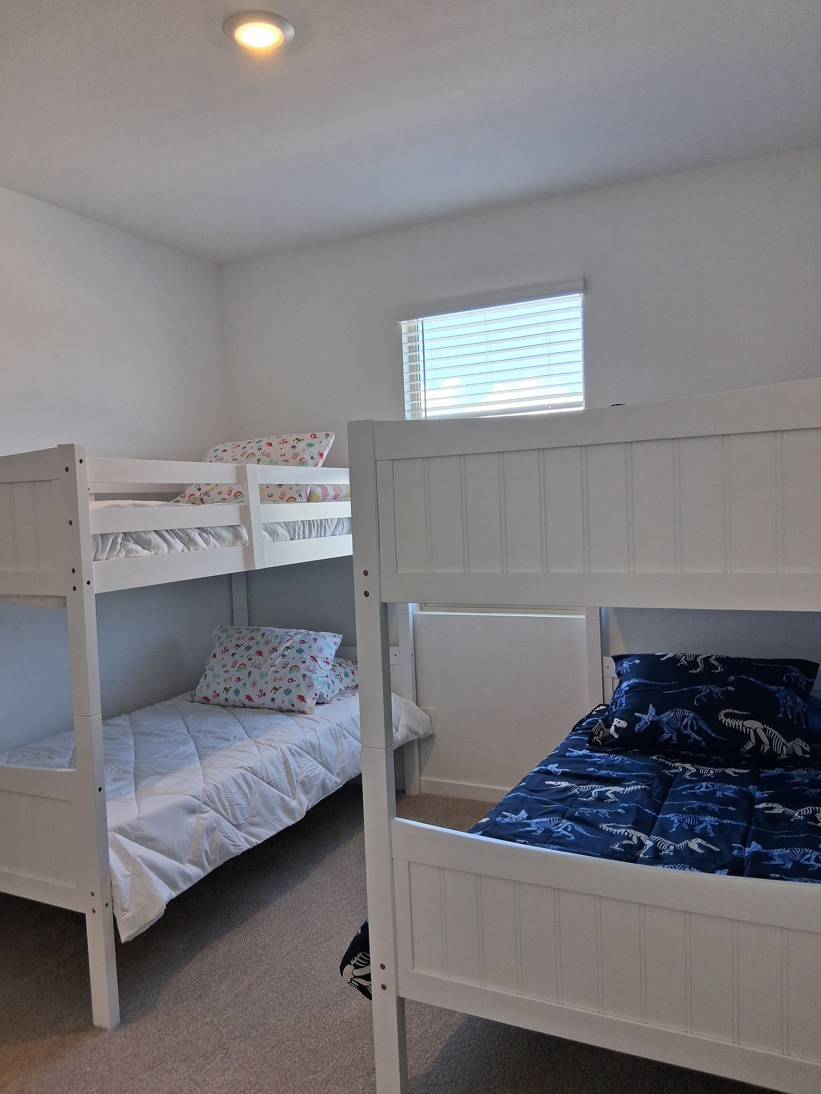 A room with bunk beds, a window with blinds, and a ceiling light.