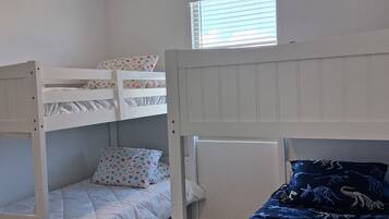 A room with bunk beds, a window with blinds, and a ceiling light.