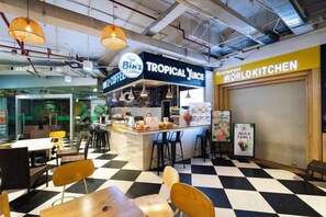 Ein Café mit kariertem Boden, einer Theke mit dem Schild 'Binz Tropical Juice' und ein im Hintergrund liegendes, geschlossenes Restaurant namens 'World Kitchen'.