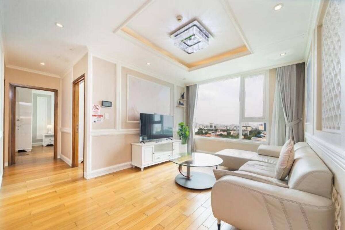 A modern living room with a sofa, a round coffee table, a TV, and a view of the city through large windows.