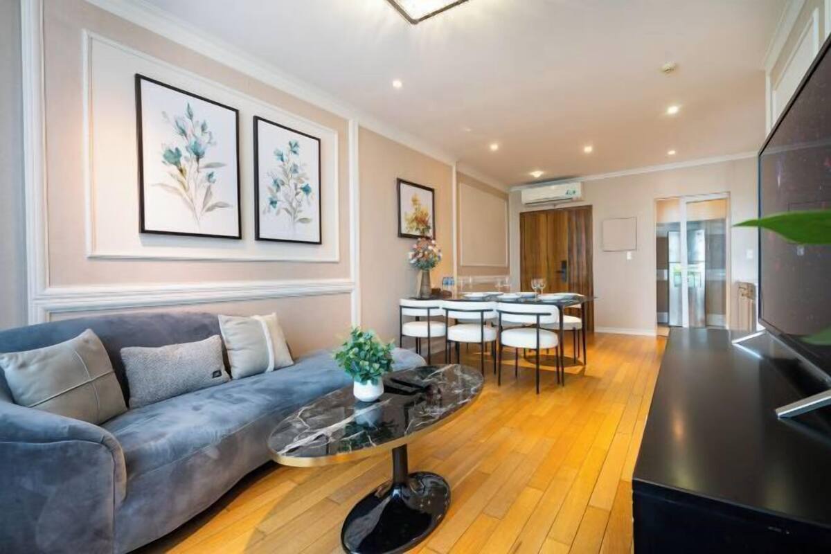 A modern living room with a grey sofa, a marble coffee table, and a dining area with a white table and chairs.