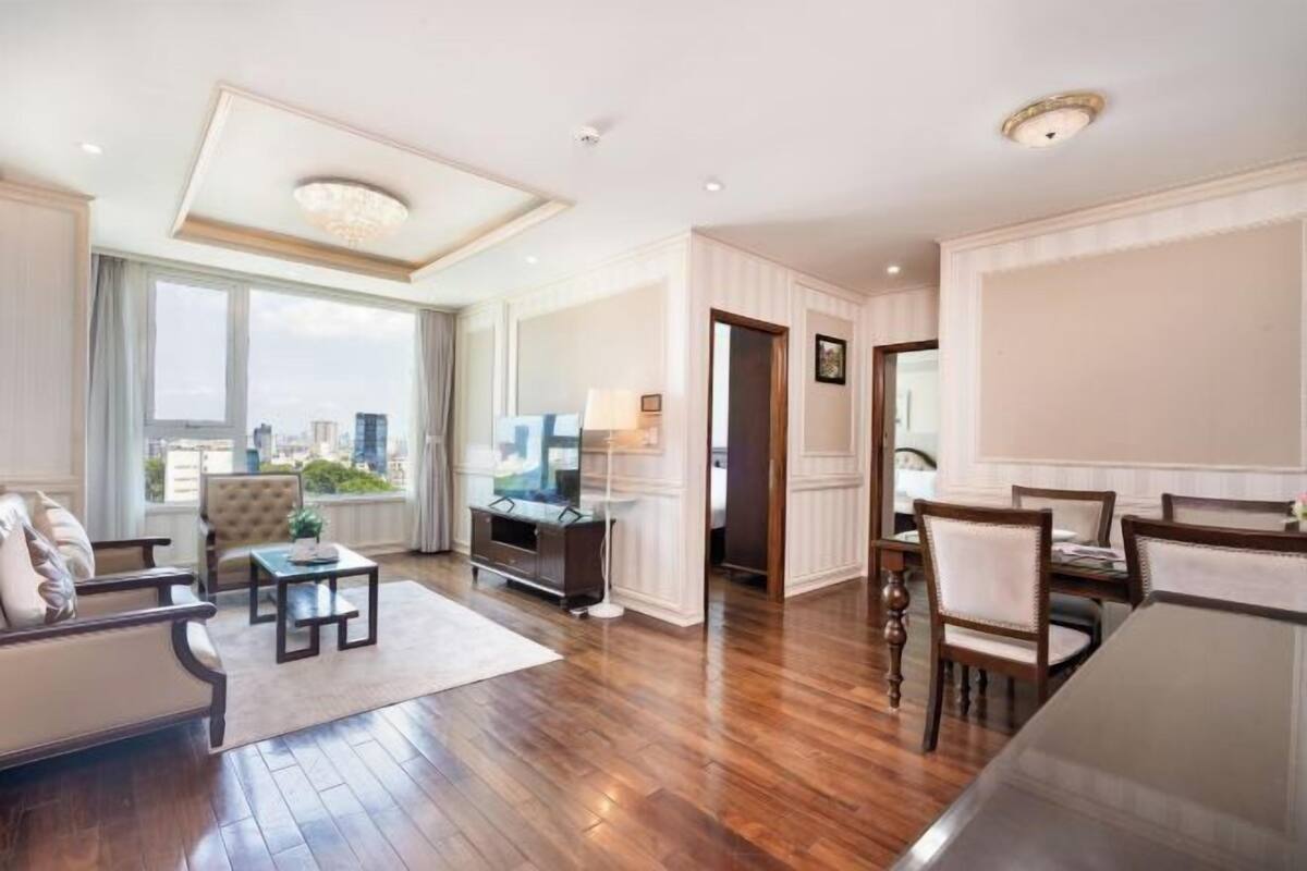 A spacious living room with a large window, a sofa, a coffee table, and a dining area with chairs.
