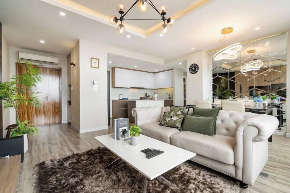 A modern living room with a sofa, coffee table, and a dining area with a chandelier.