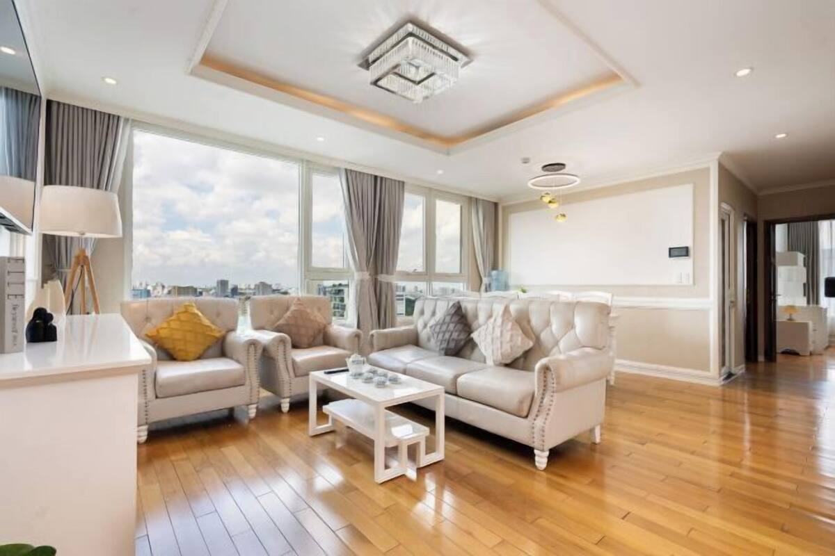 A spacious living room with a sofa set, a coffee table, and a view of the city through large windows.