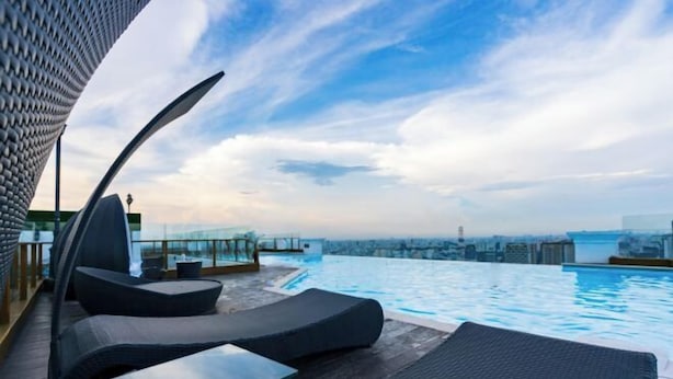 Una piscina infinita en la azotea con sillones de descanso y vistas a la ciudad.