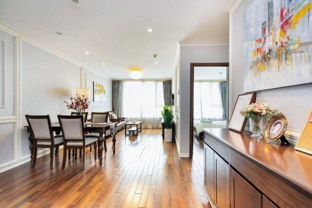 A spacious dining area with wooden flooring, a dining table, chairs, and a chandelier.