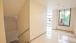 A clean, modern interior with a staircase leading to an upper floor, a large window with a view of greenery, and a polished floor. - Emerald Suites CDO (Cagayan De Oro)