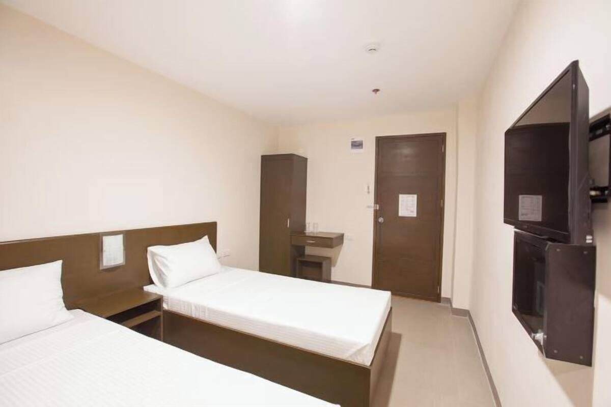 A hotel room with two single beds, a small desk, a mirror, a television, and a door.