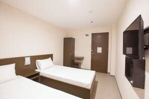 Ein Hotelzimmer mit zwei Einzelbetten, einem kleinen Schreibtisch, einem Spiegel, einem Fernseher und einer Tür.