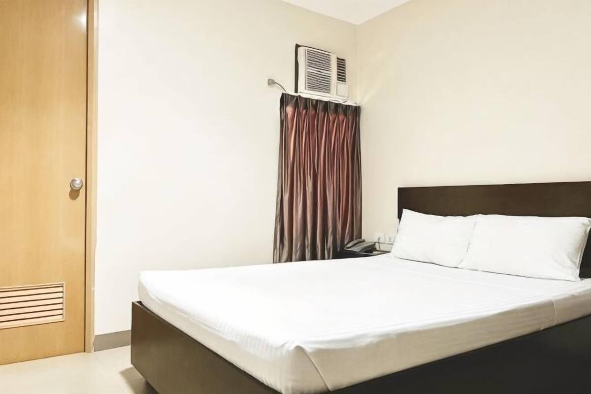 A hotel room with a bed, a door, a curtain, and an air conditioning unit.