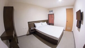 A hotel room with a bed, a TV, a wardrobe, a bedside table, and an air conditioning unit. - Emerald Suites CDO (Cagayan De Oro)