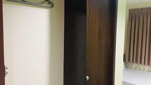 A room with a wooden door, a bed with white bedding, and a window with vertical blinds. - Emerald Suites CDO (Cagayan De Oro)
