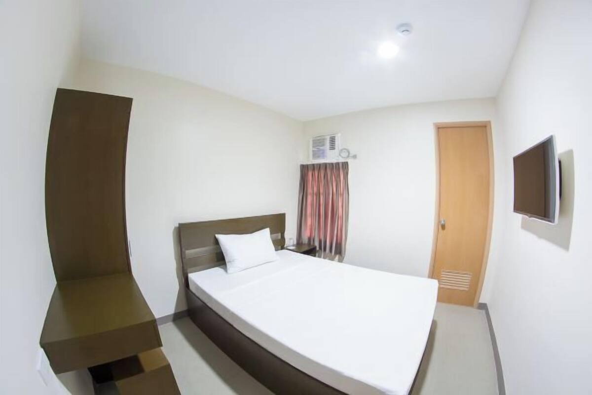 A bedroom with a bed, a TV, an air conditioning unit, and a door.