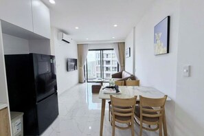 Eine moderne Küche mit einem schwarzen Kühlschrank, ein Essbereich mit Tisch und Stühlen sowie ein Wohnbereich mit Sofa und Fenster.