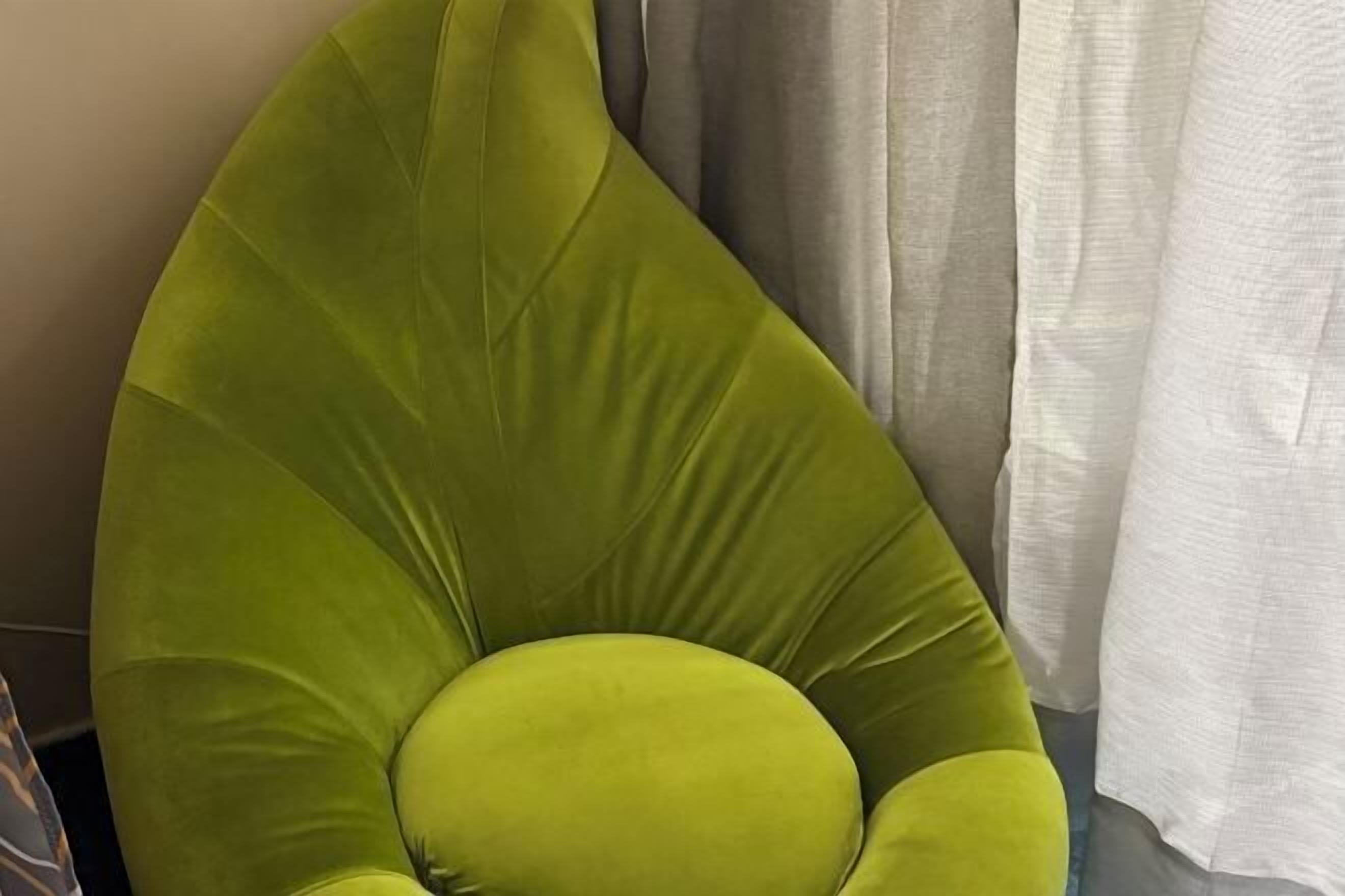 Uma cadeira estofada verde com encosto arredondado e assento acolchoado.