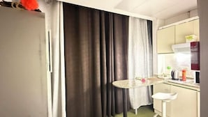 A small kitchenette with a countertop, a sink, and a window with curtains. - Rovers Hostel (Dubai)
