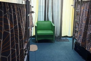 A narrow corridor with patterned curtains, a green chair, and a carpeted floor.