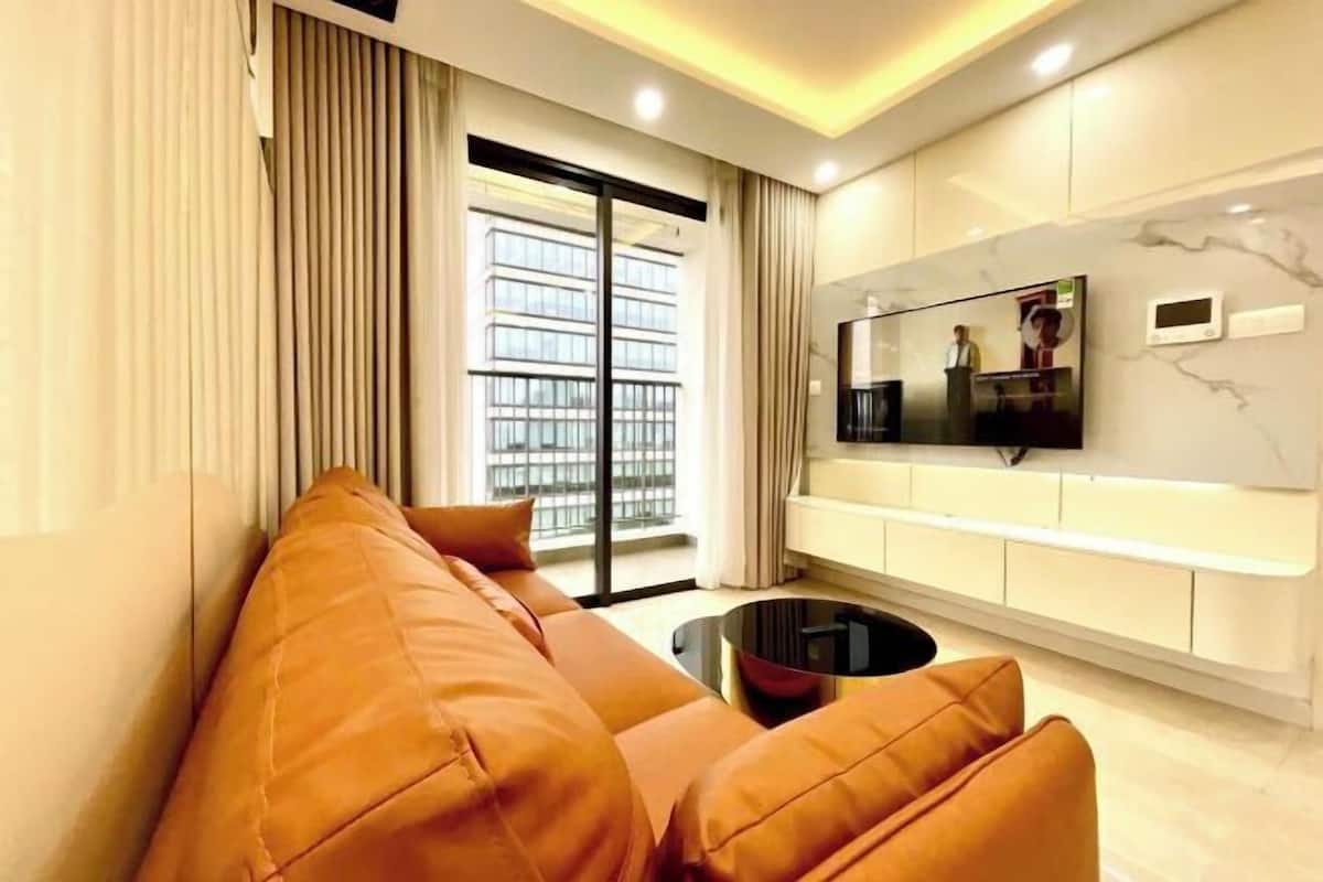 Ein modernes Wohnzimmer mit einer Couch, einem an der Wand montierten Fernseher und einer Glastür, die auf einen Balkon führt.