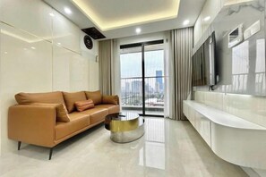 A modern living room with a sofa, a coffee table, a TV, and a large window with a city view.