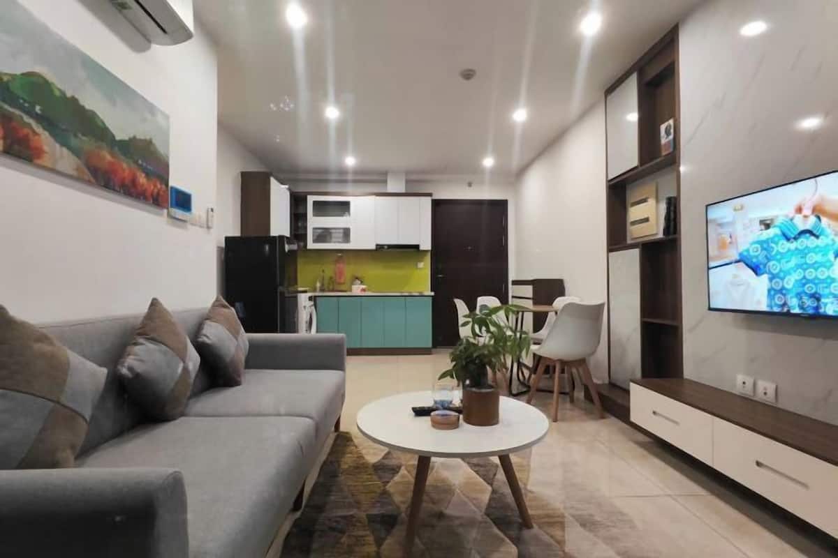 Ein modernes Wohnzimmer mit einer Couch, einem Couchtisch, einem Fernseher und einer Küche im Hintergrund.