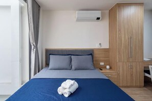 Una habitación de hotel con cama, armario, escritorio y aire acondicionado.