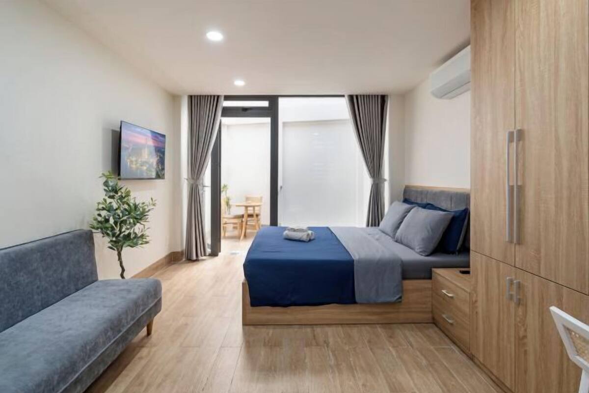 A bedroom with a bed, a sofa, a small table, a plant, and a wardrobe.