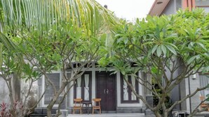 A traditional building with a stone facade, two wooden chairs on a stone bench, and a small water feature in front. - Rommeo Inn Lovina Mitra RedDoorz (Bali)
