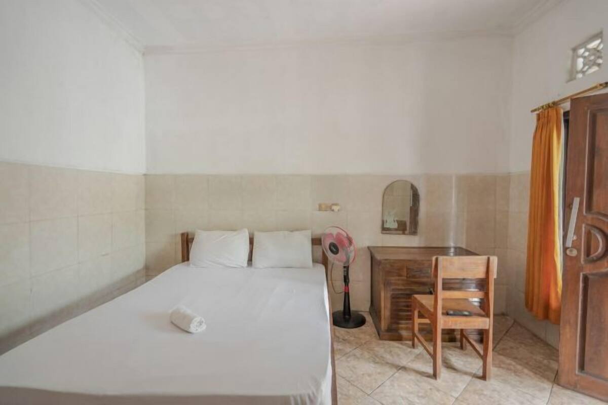 Un dormitorio con cama, escritorio, silla, ventilador y puerta con cortinas.