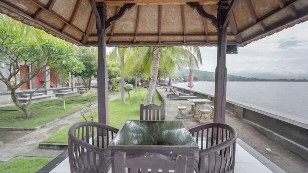 A covered outdoor seating area with a table and chairs, overlooking a body of water and greenery. - Rommeo Inn Lovina Mitra RedDoorz (Bali)