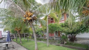 A courtyard with palm trees, a building with red and white walls, and outdoor seating. - Rommeo Inn Lovina Mitra RedDoorz (Bali)