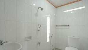 A bathroom with white tiles, a sink, a toilet, and a shower. - Rommeo Inn Lovina Mitra RedDoorz (Bali)
