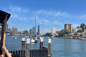 A waterfront view with boats, a city skyline, and a wooden dock. - Garden View Entire Self Contained Guesthouse (Engadine)